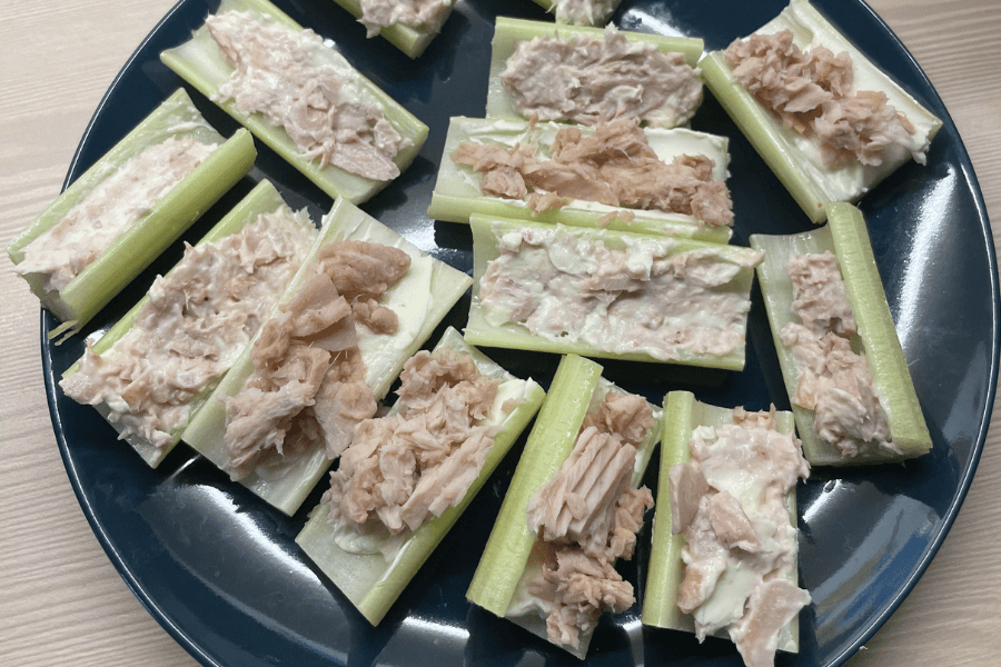 Celery sticks filled with a tuna salad mixture, arranged on a dark blue plate. The tuna appears to be mixed with mayonnaise or a creamy dressing, creating a simple, low-carb snack or appetizer.