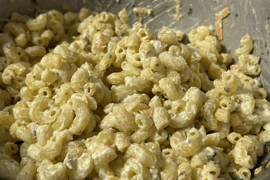 Close-up of creamy macaroni salad made with elbow macaroni, finely chopped vegetables like carrots and herbs, and a thick mayonnaise-based dressing. The salad has a rich texture and is well-mixed in a large bowl.