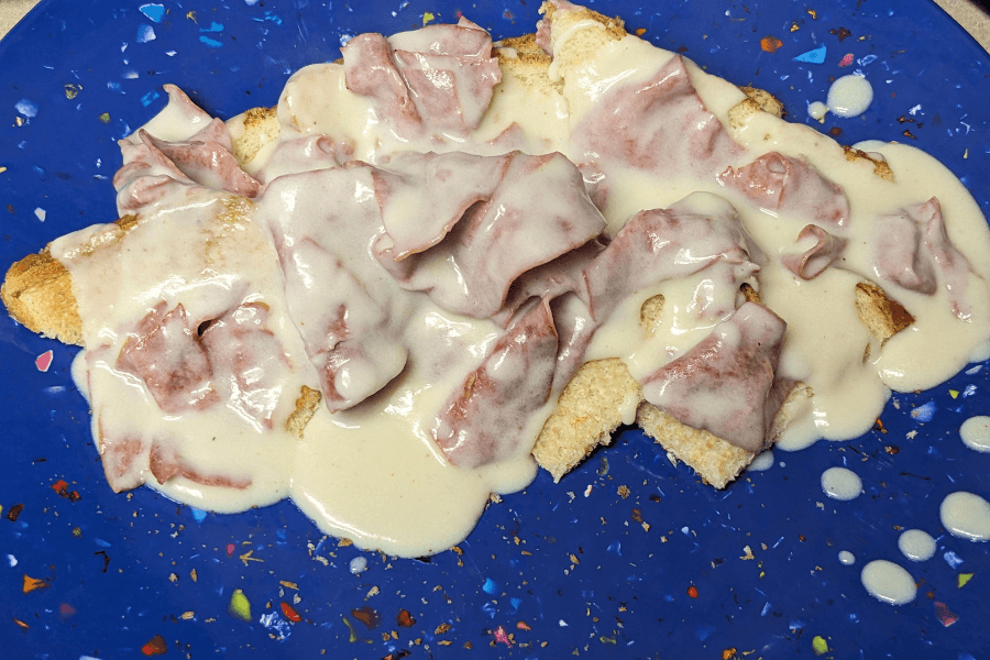 Creamed chipped beef served over toast on a speckled blue plate. The dish consists of thin slices of dried beef in a thick, creamy white sauce poured generously over toasted bread slices.