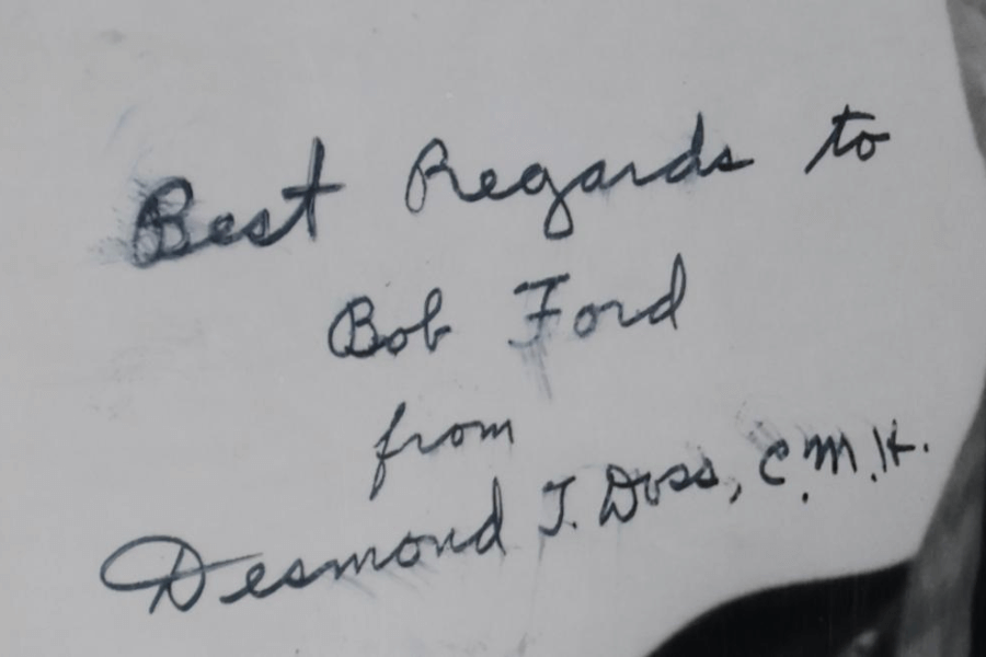 Close-up image of a handwritten note that reads: “Best Regards to Bob Ford from Desmond T. Doss, C.M.H.” The message is written in cursive with black ink on white paper, and the signature belongs to Medal of Honor recipient Desmond Doss.