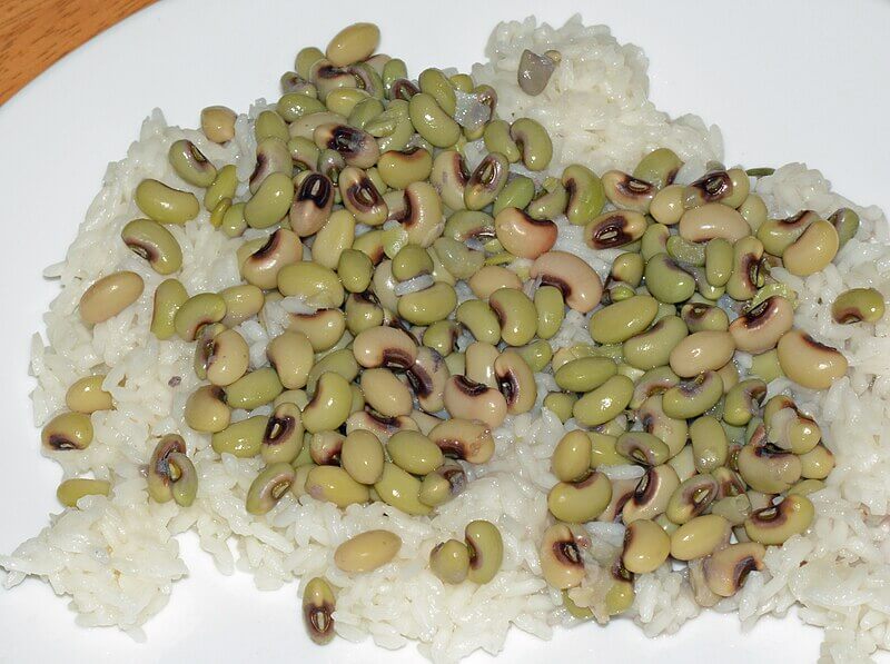 A plate of white rice topped with a generous portion of black-eyed peas. The beans are slightly glossy and pale green with dark centers, scattered unevenly over the fluffy rice.





